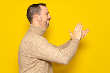 Bearded hispanic man in profile wearing brown turtleneck feeling happy, smiling and clapping hands...