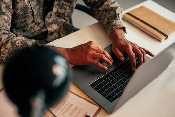 Soldier typing on laptop in office.