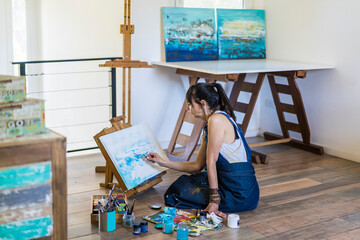 Woman artist painting on a canvas a blue abstract painting. Creative ywoman working on the floor in...