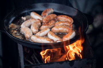 Cooking sausages on fire in a large frying pan outdoors.