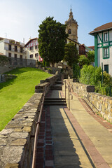 Promenade between the traditional buildings in the  old city center of Hondarribia with the tower of the church of Santa Maria de la Asuncion y del Manzano over the houses, Basque Country, Spain