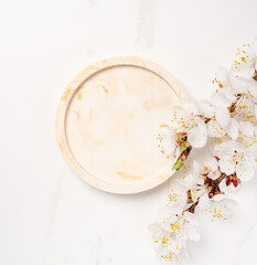 Obraz na płótnie Canvas Beauty cosmetics product presentation flat lay mockup scene made with beige marble circle shape and flowering branch of apricot tree. Studio photography.