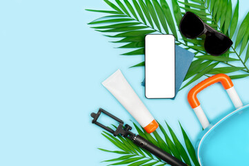 Smartphone with blank screen, selfie stick, passports, sunscreen and sunglasses on blue background....