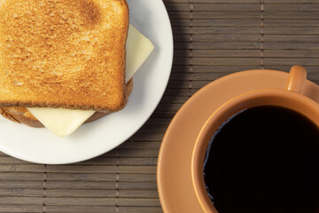 Top view a simple cheese sandwich next to a cup of coffee on a wooden placemat. Breakfast.