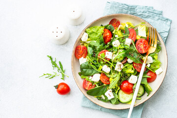 Green salad with spinach, arugula, tomatoes and feta with olive oil. Top view on white.