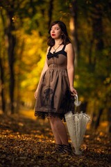 Vertical shot of a beautiful woman in a vintage dress holding an umbrella standing in a park