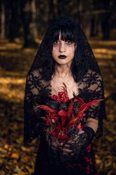 Vertical portrait of a scary corpse bride holding red flowers in the autumn forest