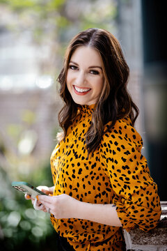 Beautiful smiling brunette Caucasian female in a leopard print shirt and blue jeans surrounded by greenery 