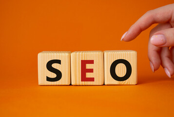 SEO - Search Engine Optimization symbol. Wooden blocks with words SEO. Businessman hand. Beautiful orange background. Business and SEO concept. Copy space.