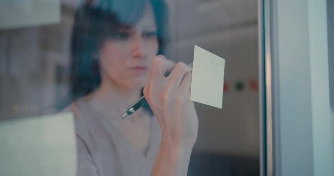 Woman make notes on stickers on window in home office, close up