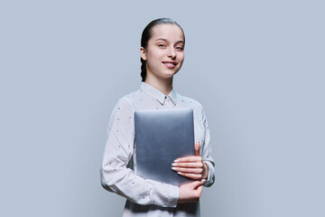 Teenage girl holding closed laptop in her hands, on grey studio background