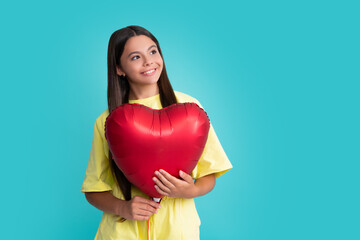 Valentines day and kids concept. Teenage girl in yellow dress with red heart-shaped balloon over blue background. Happy girl face, positive and smiling emotions.