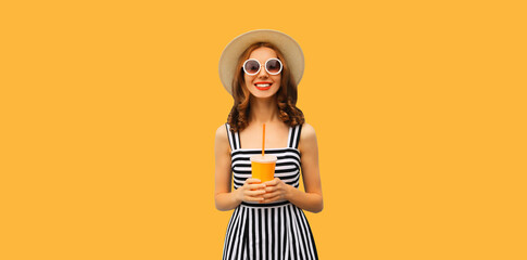 Summer portrait of happy smiling young woman drinking fresh fruit juice wearing straw round hat, striped dress on orange background