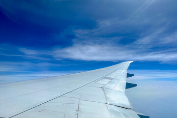 Obraz premium View from the airplane window flying above the sky with white puffy clouds, Wing of aircraft with blue sky as background.