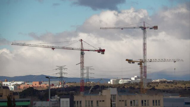An urban landscape with construction cranes, buildings and structures, mountains in the background, and flying clouds