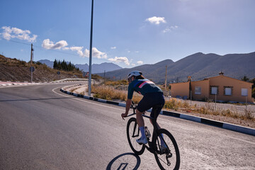 Male athlete riding time trial bicycle on empty road with a mountains in sideview. Photo of man in green jersey and white helmet. Sport goal achieving. Extremely strong motivated person
