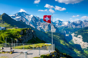 Swiss flag waving on the top of Mannlichen mountain with views of the Jungfrau region in the...
