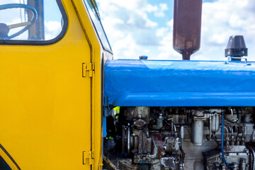 Old farm tractor painted in yellow-blue color on the field. Farm enterprise in central region of Ukraine.