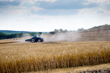 A modern blue tractor with a trailed disc harrow with a husking roller plows a field on which the...