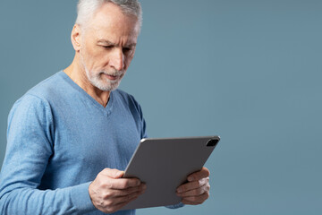 Portrait of handsome senior man holding digital tablet communication online, watching videos isolated on blue background. Technology concept