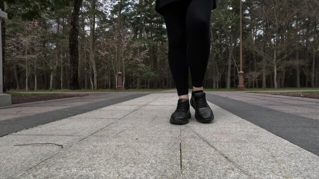 Female feet in black sneakers walk along the paths and sidewalks of city streets and parks