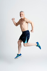 Portrait of happy senior man running isolated on white background. Handsome smiling 60 years old active male jumping high looking at camera. Sport, healthy lifestyle concept