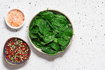 Fresh tasty baby spinach leaves with peppercorn and Himalaya salt on light marble background top view. Healthy diet food concept.