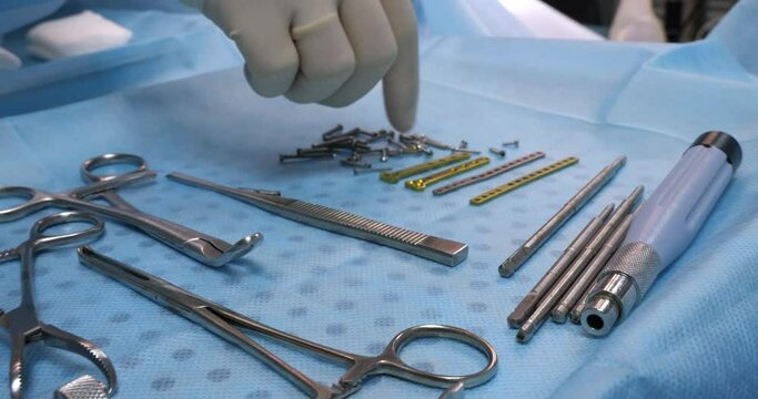 In surgery, there is an instrument for the operation on the table. The veterinarian's gloved hand goes through the screws and titanium plates on the table. A set of instruments for fracture surgery.