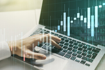 Multi exposure of abstract financial graph with hand typing on laptop on background, financial and trading concept