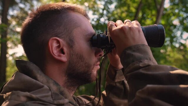 Ranger or hunter with binocular observing forest. young soldier walking through Forest near lake. Portrait close up