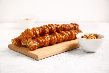 Wooden board with tasty churchkhela and walnuts on light background