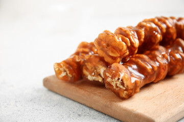 Wooden board with tasty churchkhela on light background, closeup