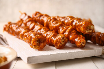 Board with tasty churchkhela on light wooden table, closeup