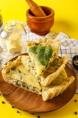 Board with pieces of delicious quiche on yellow background
