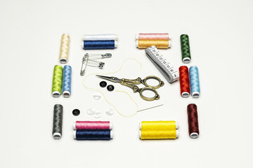 A still life with spools of colored thread with a white measuring tape, vintage seamstress scissors, needles and buttons