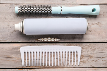 Bottle of spray, hairpin, brush and comb on light wooden background