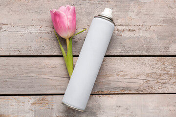 Bottle of hair spray and tulip flower on light wooden background