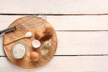 Board with glass of wheat flour, egg, bread and whisk on white wooden table
