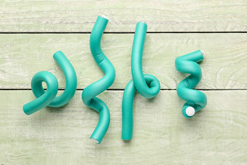 Hair curlers on green wooden background