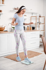 Fototapeta na wymiar Sporty young woman measuring her weight on scales in kitchen