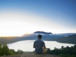person sitting on a mountain looking the buyan lake