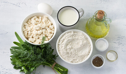 Ingredients for cottage cheese and buckwheat flatbread: cottage cheese, yogurt, green buckwheat flour, egg, vegetable oil, herbs, salt, black pepper, soda on a light blue background, top view.