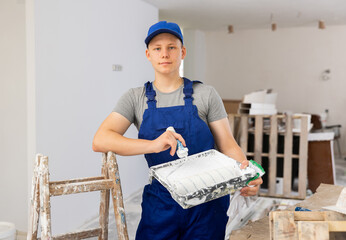 Portrait of a fifteen year old worker in uniform standing on a construction site indoors during...
