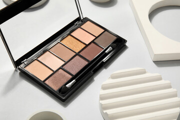 Palette of eyeshadows with brush and podiums on light background, closeup