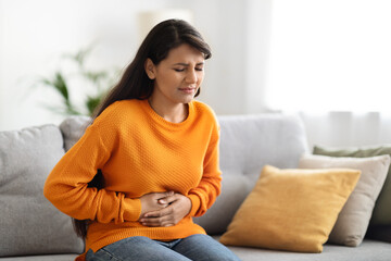 Concerned indian woman suffering from stomach-ache at home - obrazy, fototapety, plakaty