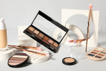 Decorative cosmetics with eyeshadows, brushes and podiums on light background