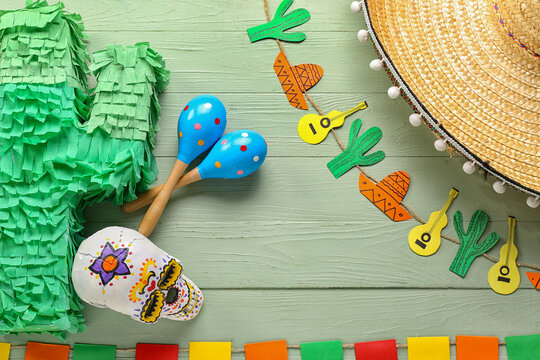 Frame made of Mexican maracas, painted skull, pinata and garland on green wooden background