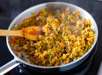 Closeup of braised white cabbage, stewed with carrots and onions in a pan on a kitchen stove