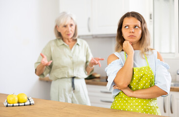 Offended young woman listening her senior mother standing behind and quarreling with her.