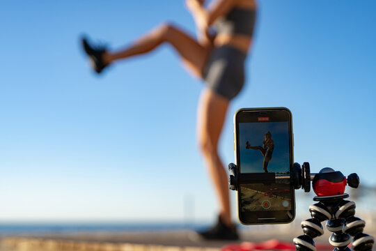a beautiful girl goes in for sports does functional training exercises on the seashore at dawn and takes pictures of herself on the phone. stream. online training